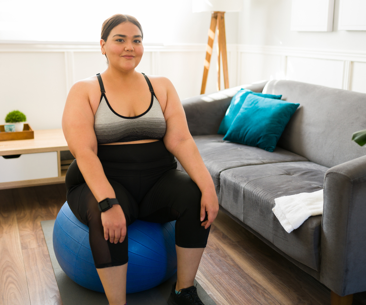 A woman sits atop an exercise ball, dressed for a workout, in her home.